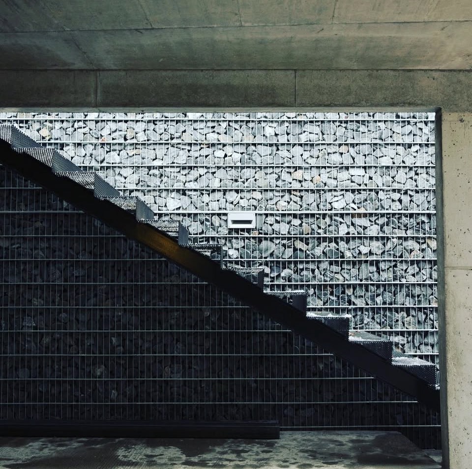 Black steel staircase with grated treads against a gabion stone wall