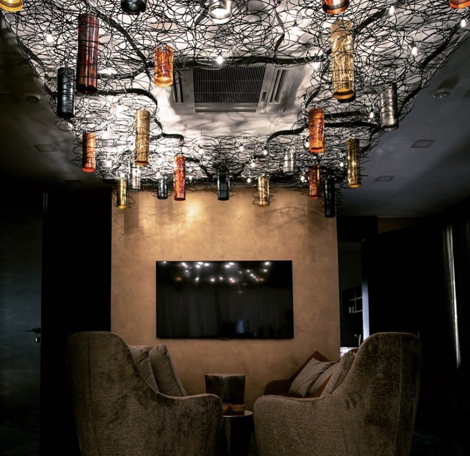 Ceiling installation of tangled wire and metal-cylinder lamps over a dark lounge