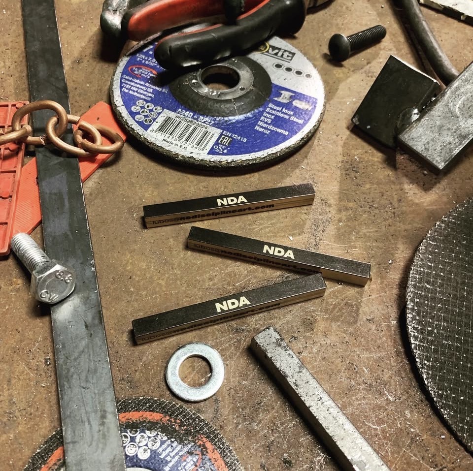 Workshop bench with NDA-branded steel billets, grinding discs and tools